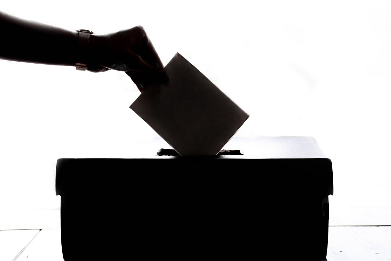 who-we-are Silhouette of a hand placing a vote into a ballot box, symbolizing democracy.
